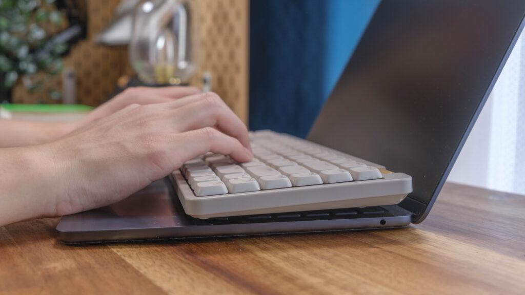 ノートパソコンの上に外付けキーボードを乗せて作業している様子