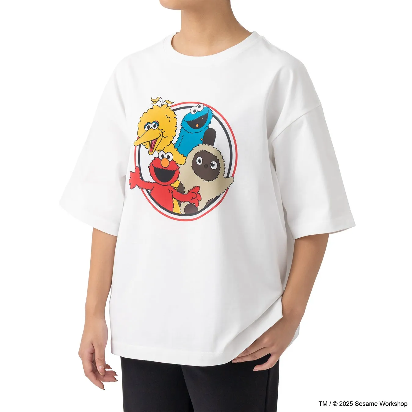 白いTシャツを着た女性。Tシャツには、セサミストリートのキャラクター、エルモ、クッキーモンスター、ビッグバード、そして何人かの他のキャラクターが描かれています。