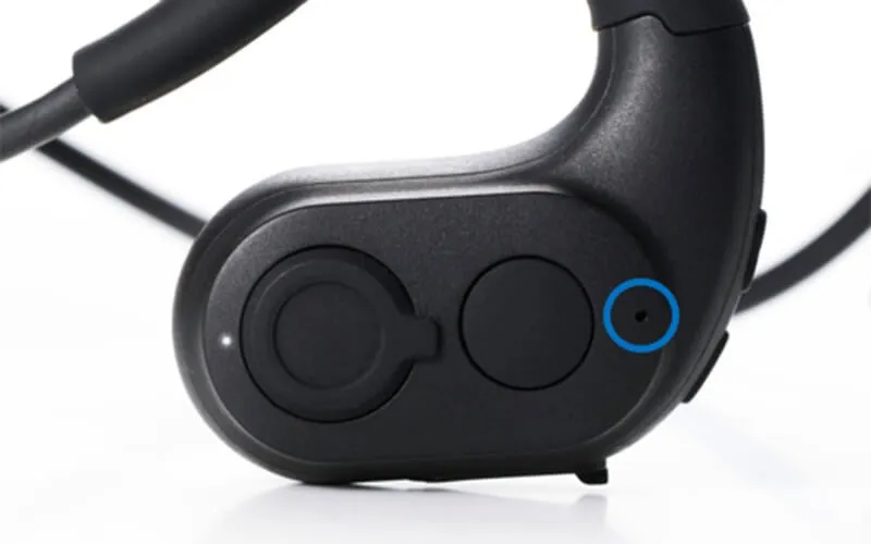黒いイヤホンのクローズアップ写真です。イヤホンには2つの丸いボタンがあり、そのうちの1つには小さな穴があります。イヤホンは白い背景にあります。