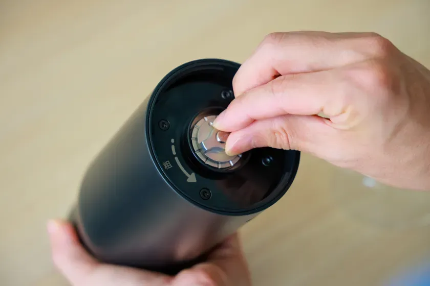 黒い容器の蓋部分を調整している手元の写真です。