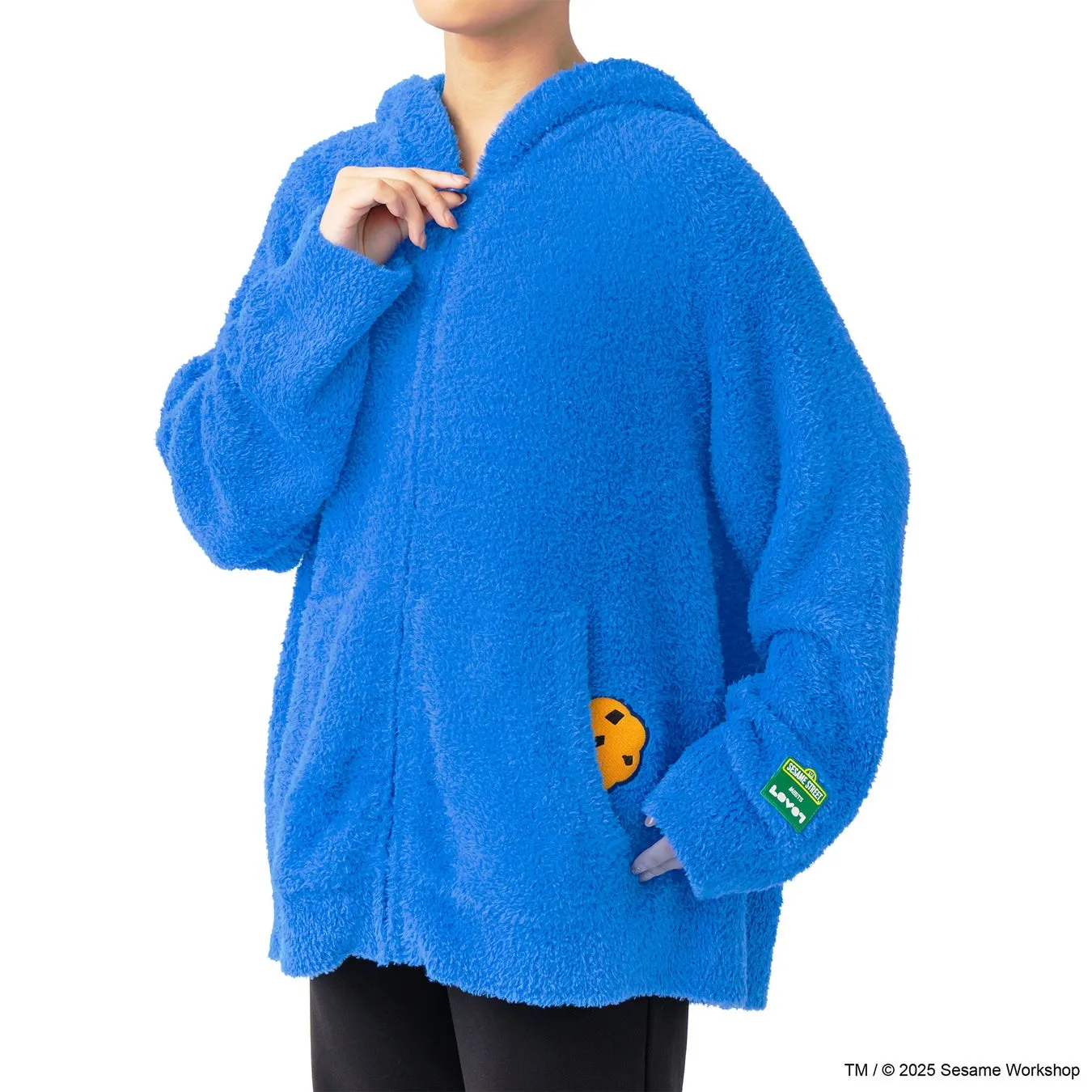 青いフリース素材のフード付きパーカー。ポケットにクッキーのワッペンがあり、袖にはセサミストリートのロゴが付いている。人物が着用している様子が写っている。