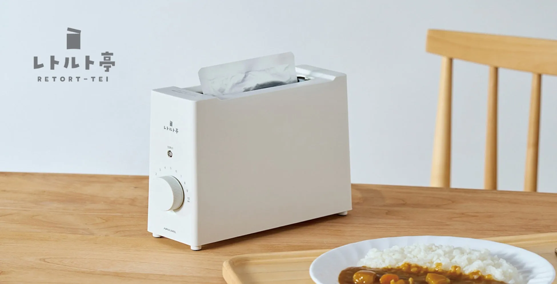 レトルト食品を温めるための家電製品の写真です。白い本体に、レトルト食品を挿入して温める仕組みのようです。食事としてカレーライスが添えられています。